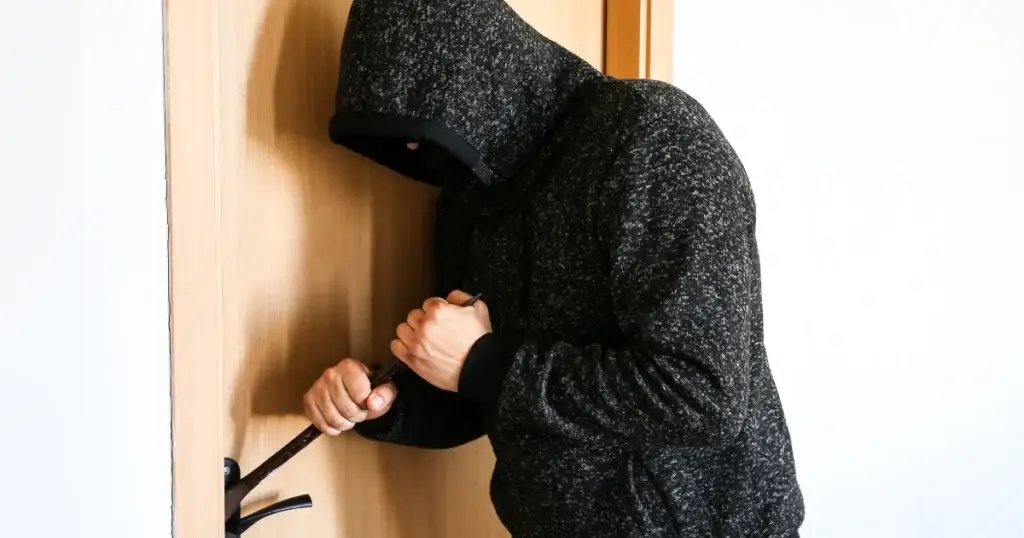 Persona encapuchada intentando entrar por la fuerza en una vivienda, imagen del delito de usurpación y la necesidad de aplicar la nueva ley antiokupas.