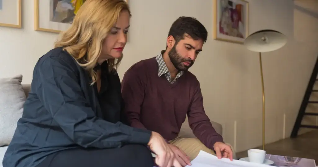 Dos personas revisando planos de vivienda en una reunión, representando las consecuencias legales de la ocupación de una vivienda habitual.